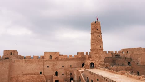 view of ancient ribat of monastir fortress with tower and flag of tunisia