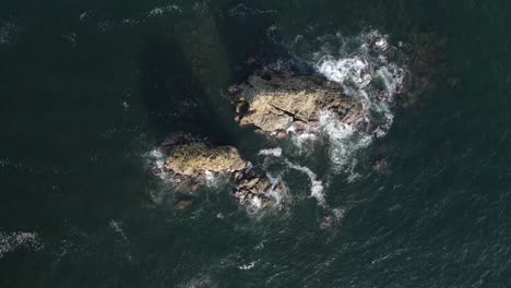 Vista-Aérea-De-Las-Olas-Rompiendo-En-Dos-Grandes-Rocas-En-La-Playa-De-Manuel-Antonio-En-Quepos,-Costa-Rica,-Vista-Panorámica-De-Arriba-Hacia-Abajo