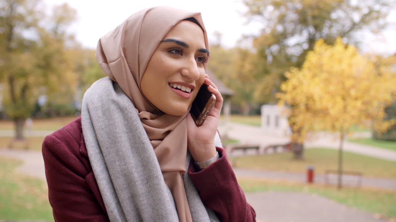 British Muslim Woman Using Mobile Phone In Park