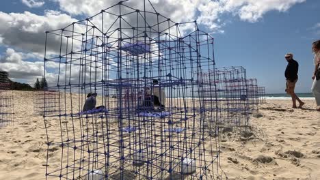 personas interactuando con esculturas de alambre en la playa