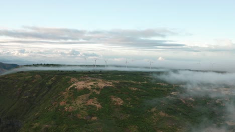 Aéreo-En-Medio-De-La-Montañosa-Madeira-Con-Nubes-Bajas-Y-Molinos-De-Viento-Distantes