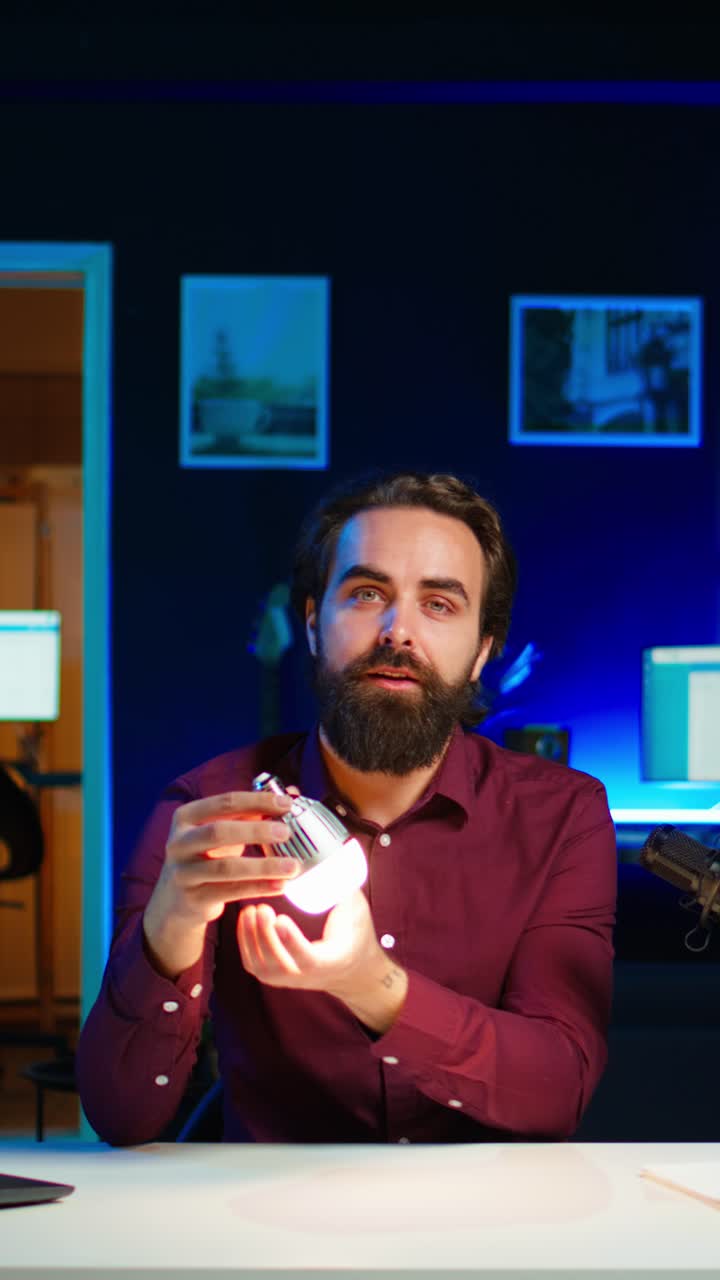 Guru di tecnologia che realizza video verticali in un appartamento studio scarsamente illuminato, mentre filma una recensione di una lampadina smart.