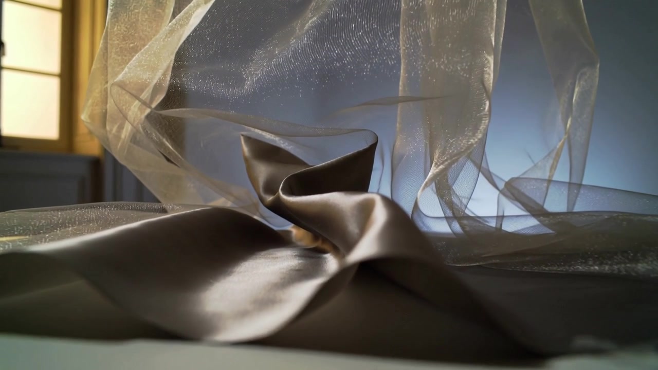 Tecido transparente com brilho sendo levantado, brisa da janela movendo-se sobre o cetim em um pedestal no estúdio, formando uma dobra central.