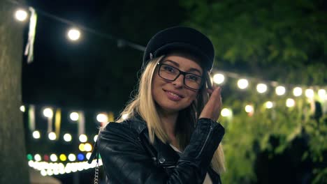 Portrait-Of-A-Beautiful-Girl-In-Stylish-Hat,-Fashion-Glasses-And-A-Black-Leather-Jacket-Walks-In-The-Night-Park