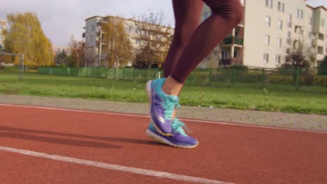 Vista-De-Las-Piernas-De-Una-Chica-Con-Zapatos-Para-Correr-Calentándose-Para-Correr-En-Una-Pista-De-Atletismo-En-Cámara-Lenta