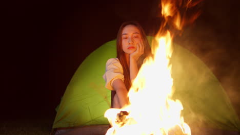 close up portrait of asiatic young woman camping at night in front of bonfire