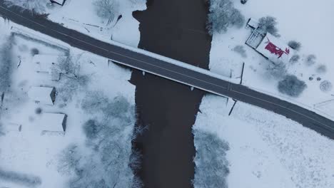 Paisaje-Cubierto-De-Nieve-Con-Puente-Sobre-El-Río-Abava-Cerca-Del-Pueblo-De-Renda,-Vista-Aérea-De-Pájaro