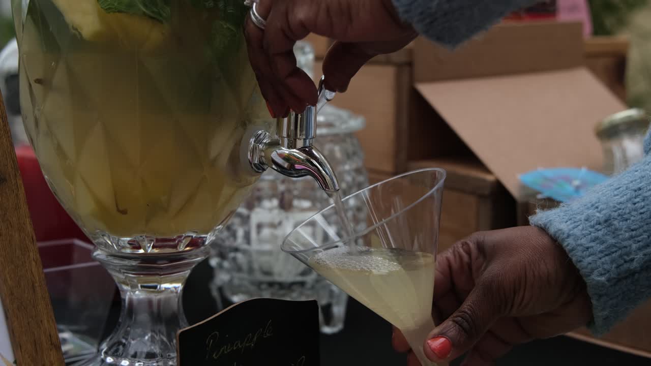 A black woman pours herself a mojito through a container at local market stall.