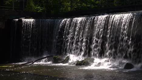 static view of man made waterfall gently falling on rocks and trees in park setting