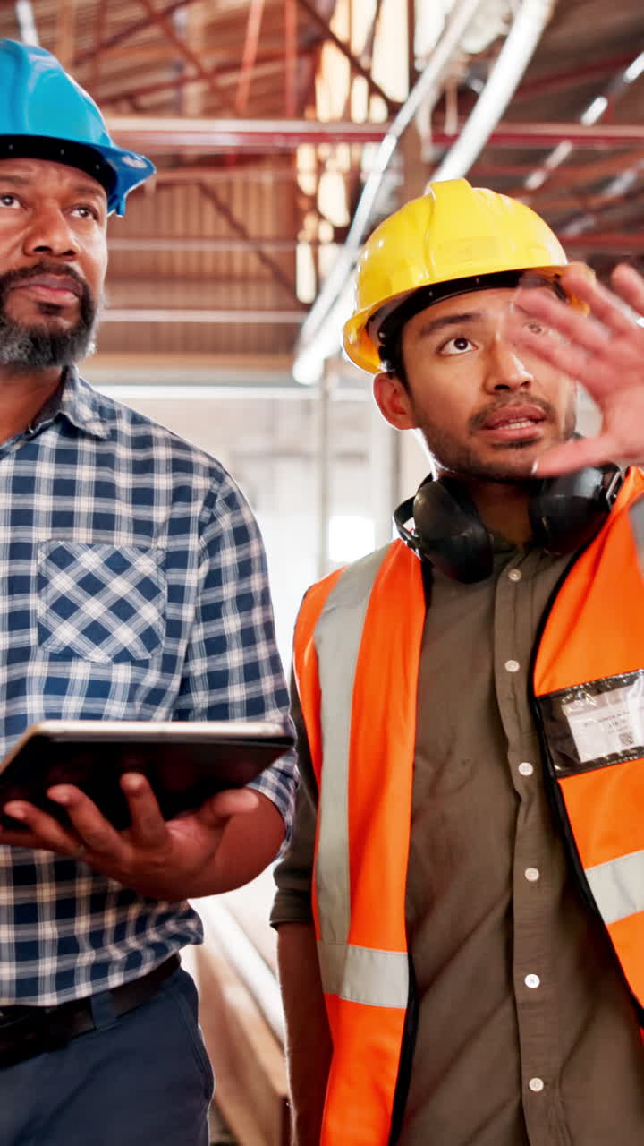 Two Male Workers in Safety Gear Discussing Plans in a Factory