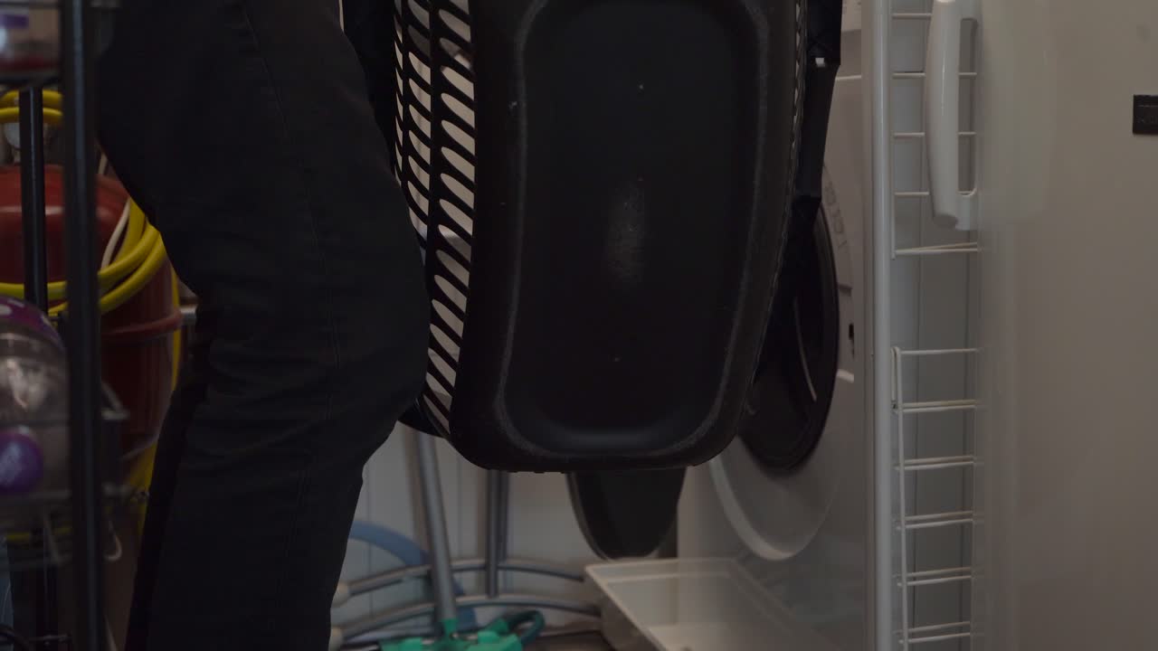 남자는 세탁기에 짐을 싣고 세탁 바구니를 들고 방을 나간다