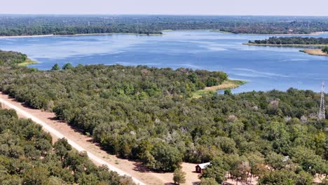 Moving-back-and-slowly-descending-above-a-large-swath-of-trees-on-the-edge-of-a-pretty-blue-lake