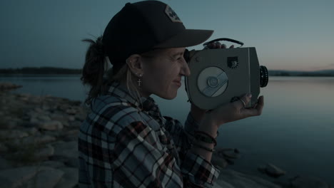 woman filming sunset over lake with retro video camera