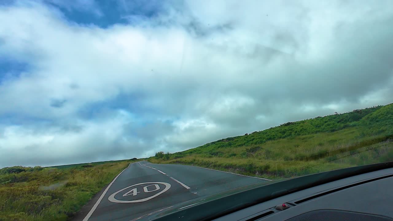 Driving POV Along Winding Open Country Road with Dynamic Cloudscape Sky and Plant Life Over Open Countryside Landscape in Wales, UK. Travel Transportation Clip
