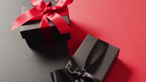 Close-up-of-two-black-gift-boxes-with-red-and-black-ribbons-on-black-and-red-with-copy-space