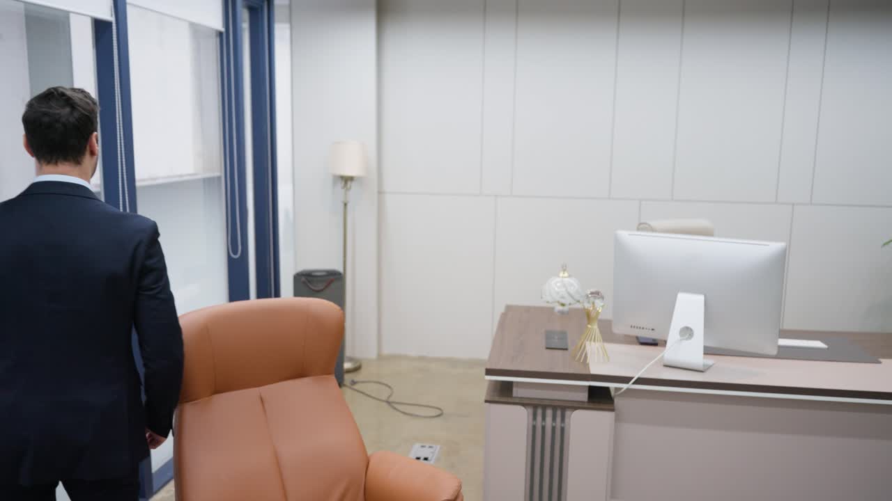 CEO businessman walks through his luxury spacy office room, sits by a sleek desk and computer, takes documents out of a folder and reviews paperwork charts and graphs - slow motion, follow shot