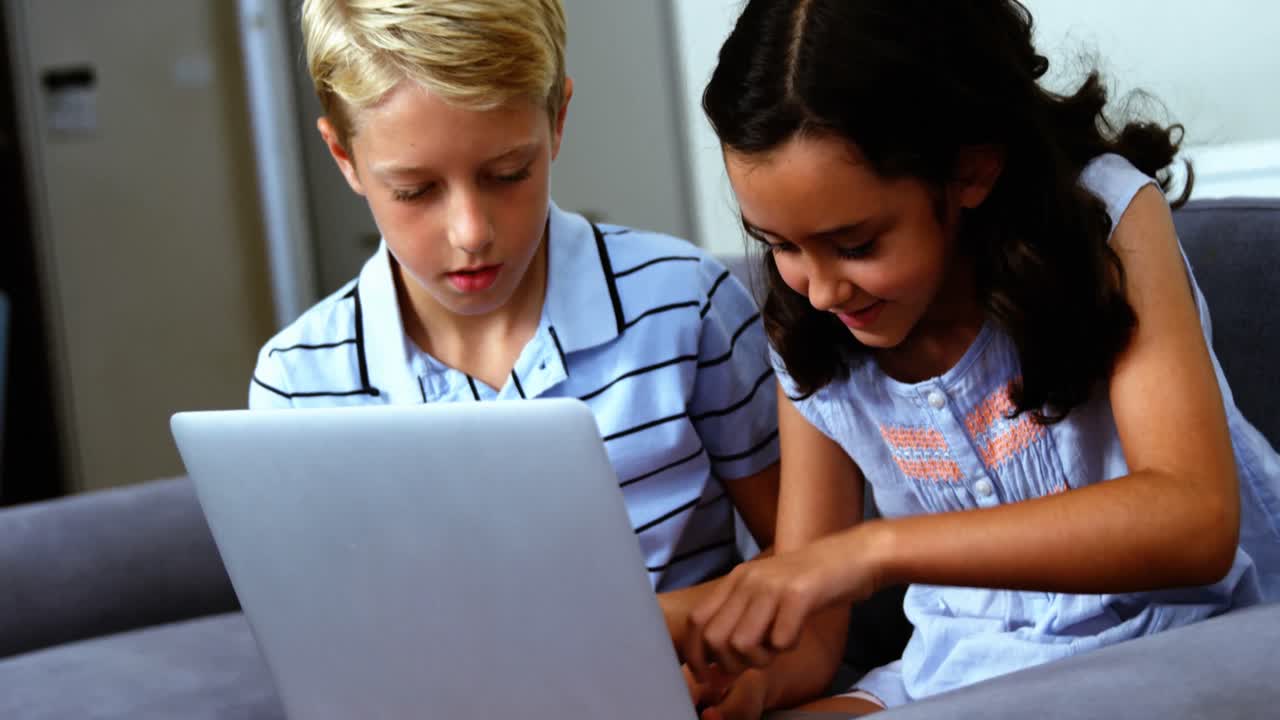 Siblings using laptop in living room
