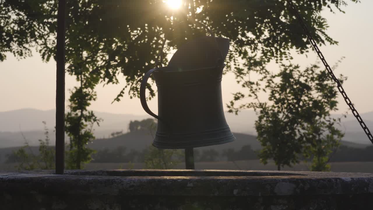 Primo piano di un vecchio secchio di metallo nella campagna toscana, Italia, con la luce del sole proveniente dalle colline panoramiche.