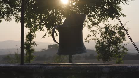 Un-Viejo-Cubo-De-Metal-Cerca-De-La-Campiña-De-Toscana,-Italia,-Con-El-Sol-Desde-Las-Pintorescas-Colinas-Del-Paisaje