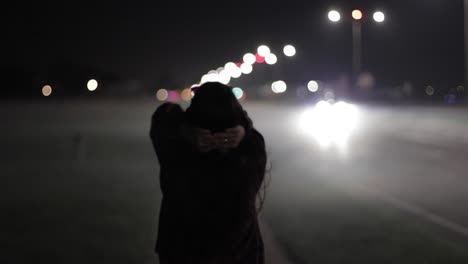 young woman walking through the streets at night clutching her hands behind her head