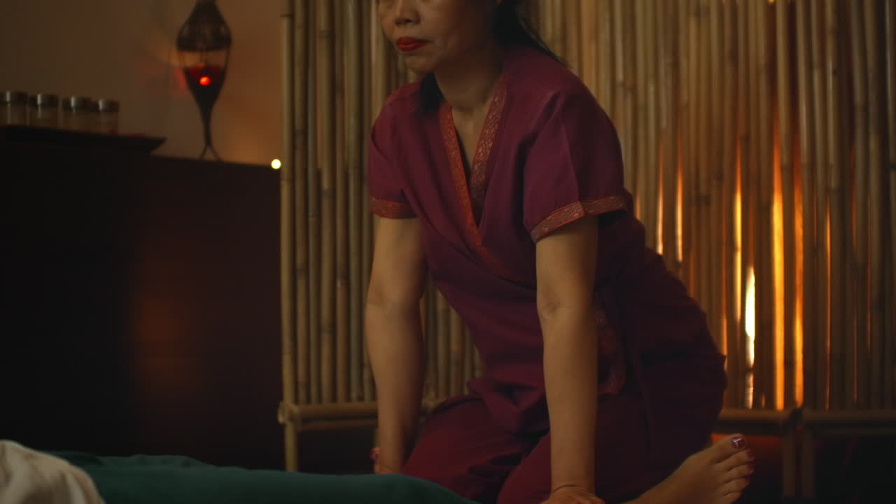 Asian performs massage in national clothes of Thailand. Asian Spa salon in Europe. Young Caucasian woman relaxes while performing massage.