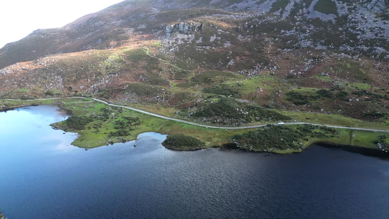 Wide rotating drone shot of Gap of Dunloe, Bearna or Choim&iacute;n, mountain pass in County Kerry, Ireland with the lake shoreline