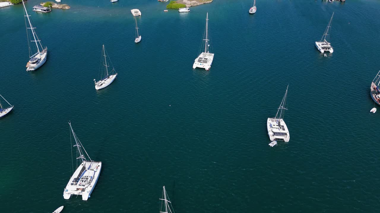 Top-down aerial of multiple sailboats anchored in calm ocean waters, creating a peaceful and scenic view