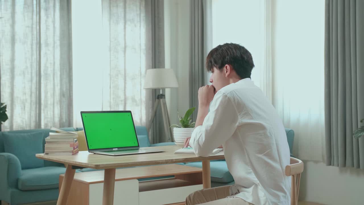 Side View Of Asian Man Student Being Sleepy While Looking At Green Screen Computer At Home