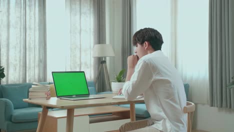 side view of asian man student being sleepy while looking at green screen computer at home