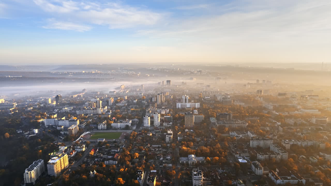 Aerial drone timelapse view of Chisinau at sunrise, Moldova. View of the city with fog in the air, multiple buildings, squares and streets with yellowed trees