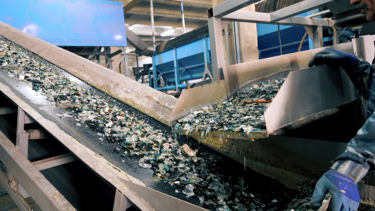 Worker in special gloves sorting glass garbage on a vibrating conveyor belt at waste sorting plant