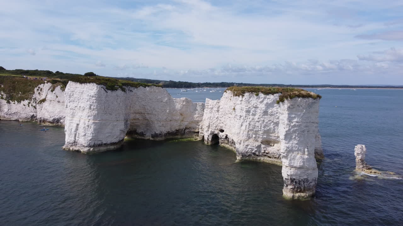 Aerial flying towards chalk rock formation, revealing boats in background, UK