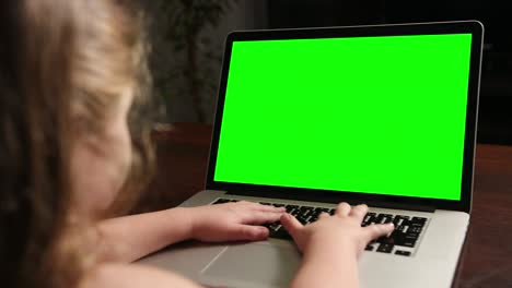 sobre el hombro la niña utiliza una computadora portátil con una maqueta de pantalla verde en exhibición.