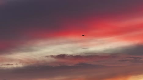 large cargo plane flying through bright pink fluffy clouds at sunset static aerial telephoto