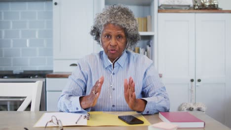 Portrait-of-senior-african-american-female-doctor-wearing-earphones-talking-while-having-a-videocall