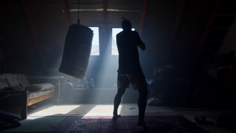 man training with punching bag in attic