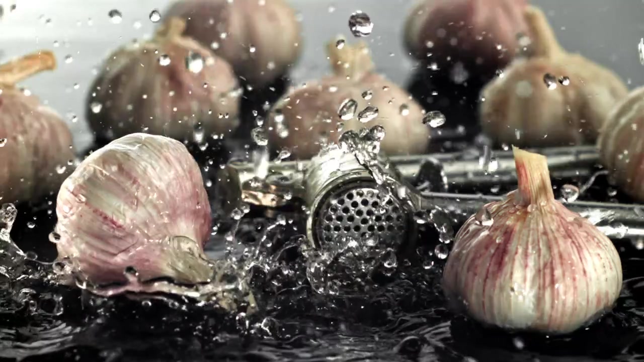 Bulbes d'ail frais et presse-ail avec des éclaboussures d'eau.