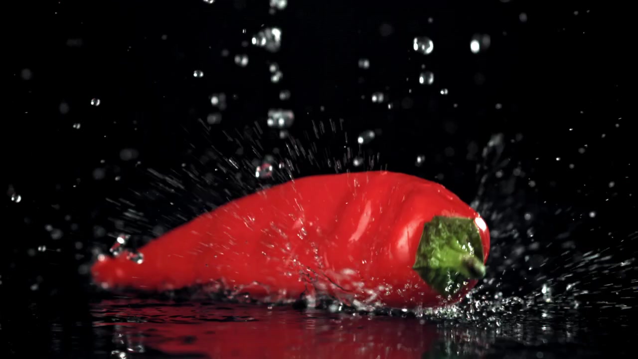 Červená chilli paprička padající zpomaleně do vody s cákanci.