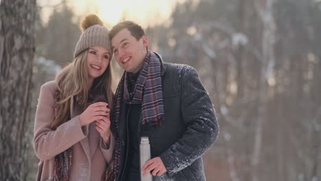 couple in love in the winter forest to drink tea from a thermos. stylish man and woman in a coat in the park in winter for a walk.