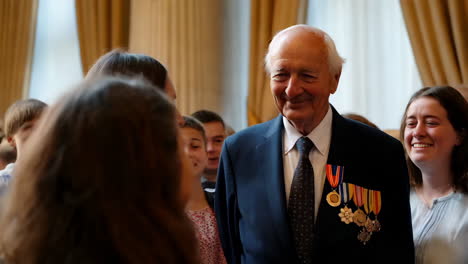 elderly man adorned with medals surrounded by smiling young people at a formal event