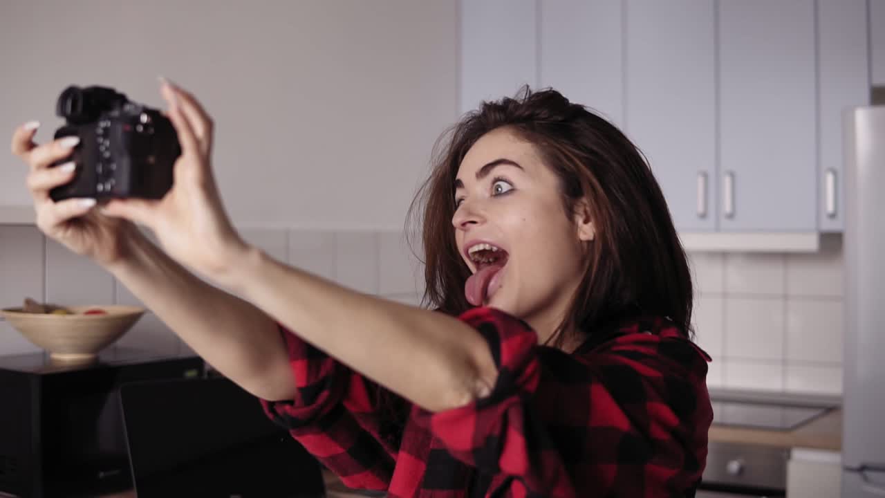 Giovane ragazza bruna attraente che fa una faccia buffa mentre cerca di farsi un selfie con una macchina fotografica professionale