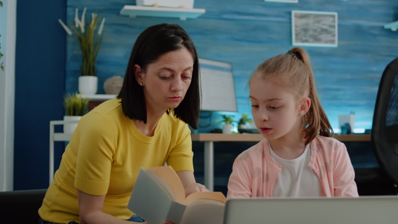Pupil using laptop and notebook for homework with help from mother