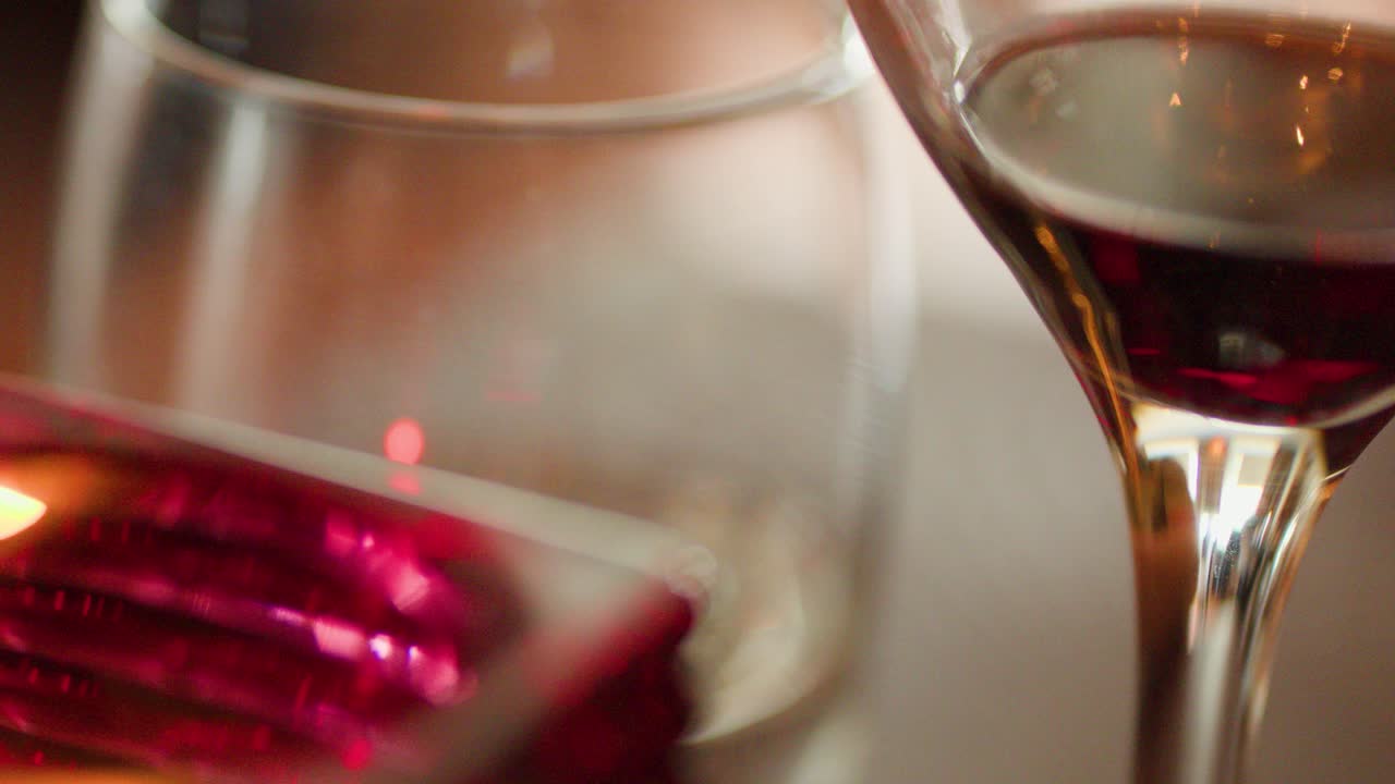 Close-up of red wine glass, candle, and glassware in warm, intimate restaurant lighting