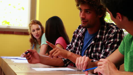 Students-sitting-in-a-line-writing-and-chatting-in-classroom