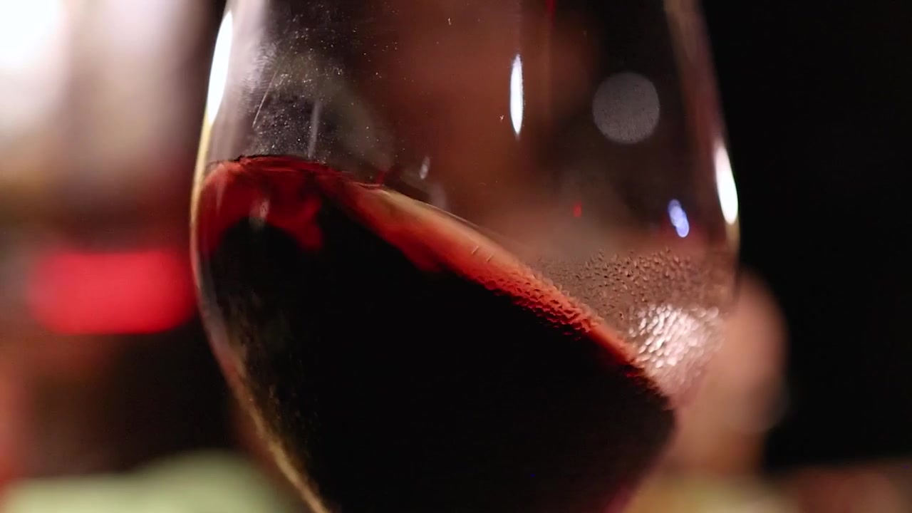 Una macro in dettaglio mostra vino rosso scuro che vortica all'interno di un bicchiere con condensa