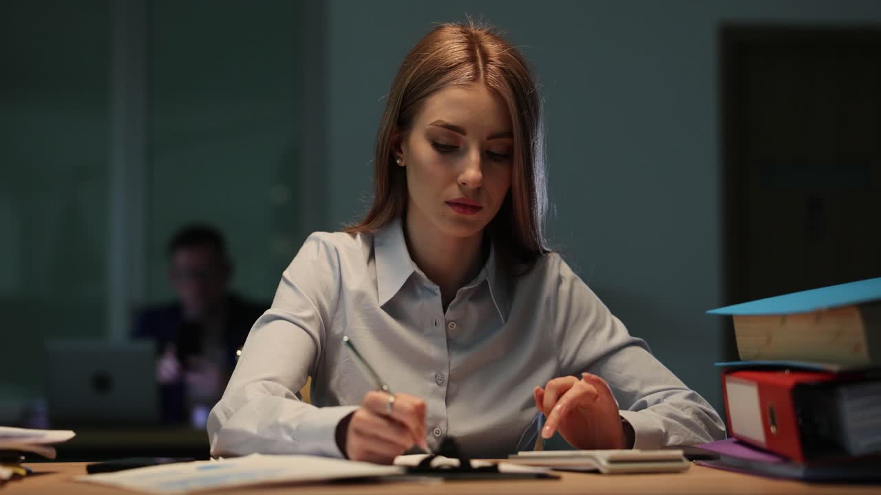 Jovem mulher trabalhando intensamente em sua mesa em um escritório mal iluminado
