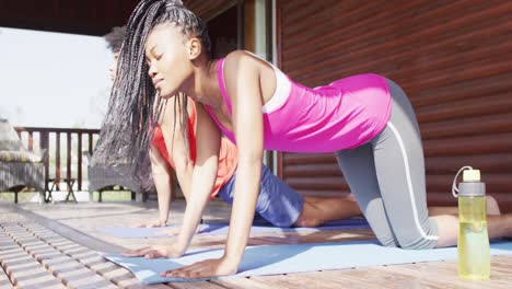 una feliz pareja afroamericana haciendo yoga y estirándose en una cabaña de madera, cámara lenta