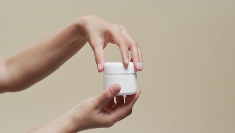 hands of woman holding cream on beige background with copy space, slow motion