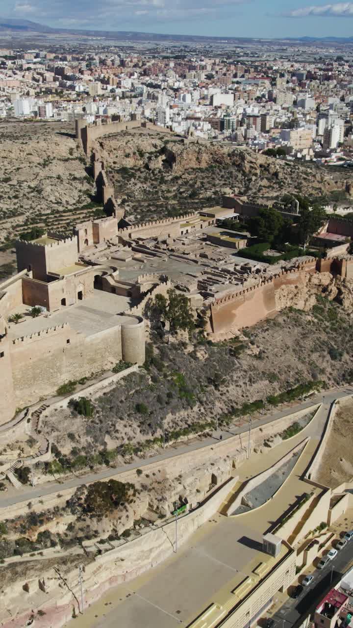 Arco aereo verticale che cattura l'Alcazaba di Almería in cima alla collina, mostrando le sue mura fortificate e la posizione strategica