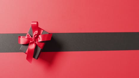 overhead view of black gift box with red ribbon on black and red background with copy space